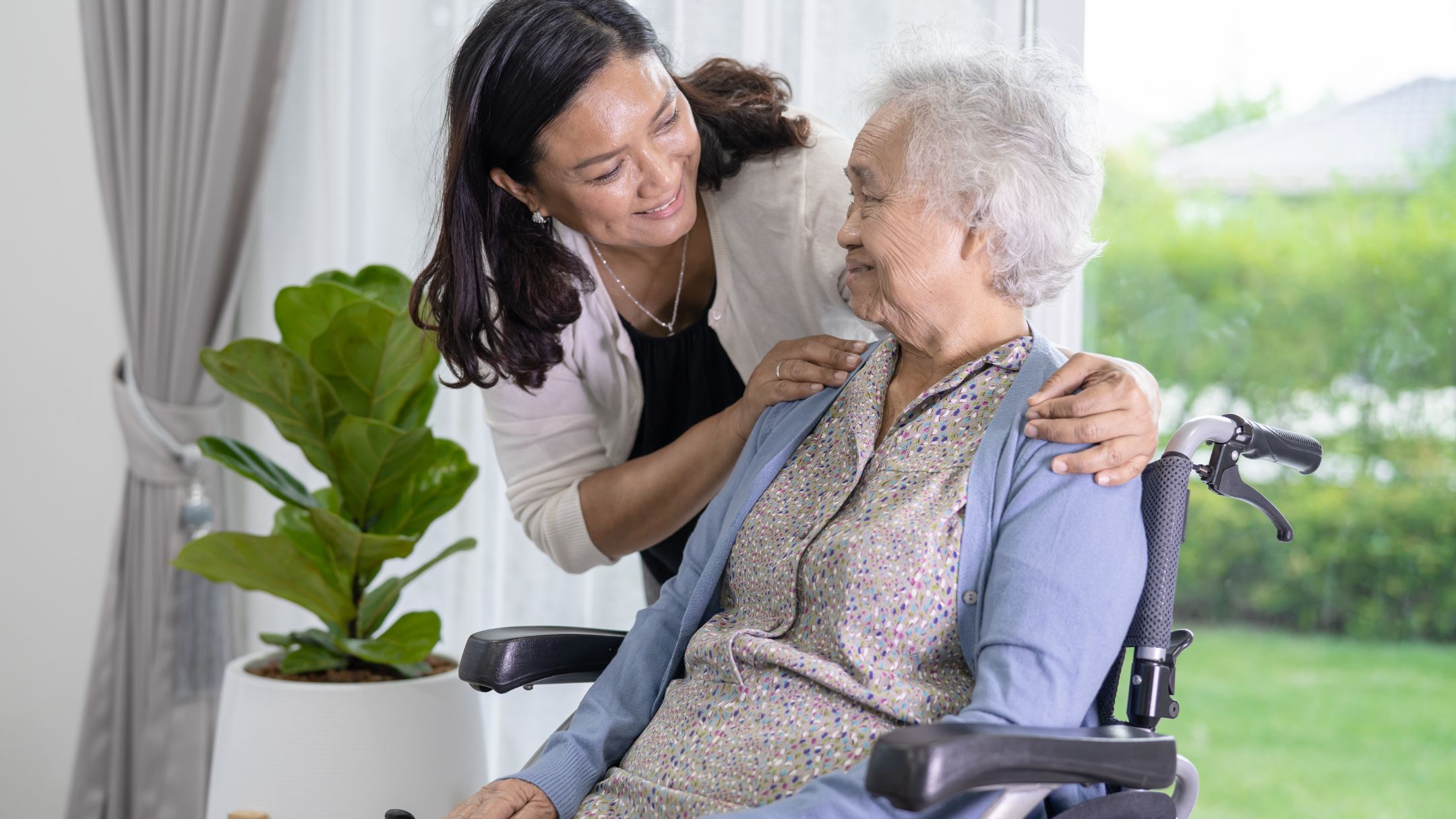 Caregiver smiling warmly with elderly woman in wheelchair at home